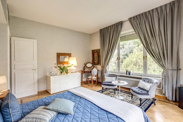 Une chambre à coucher avec un grand lit, un bureau, une chaise, un radiateur et une fenêtre avec des rideaux.