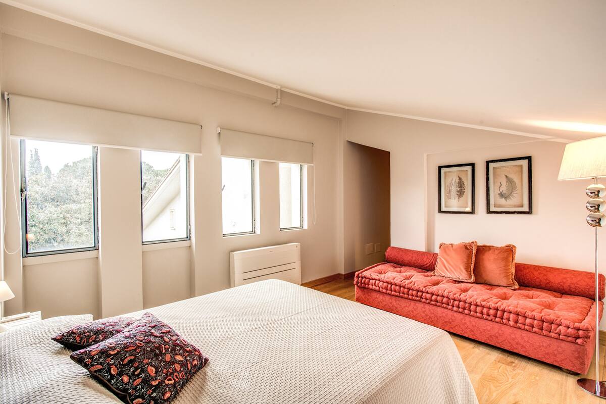 Ein Schlafzimmer mit einem Bett, einem roten Sofa und zwei Fenstern mit Jalousien.