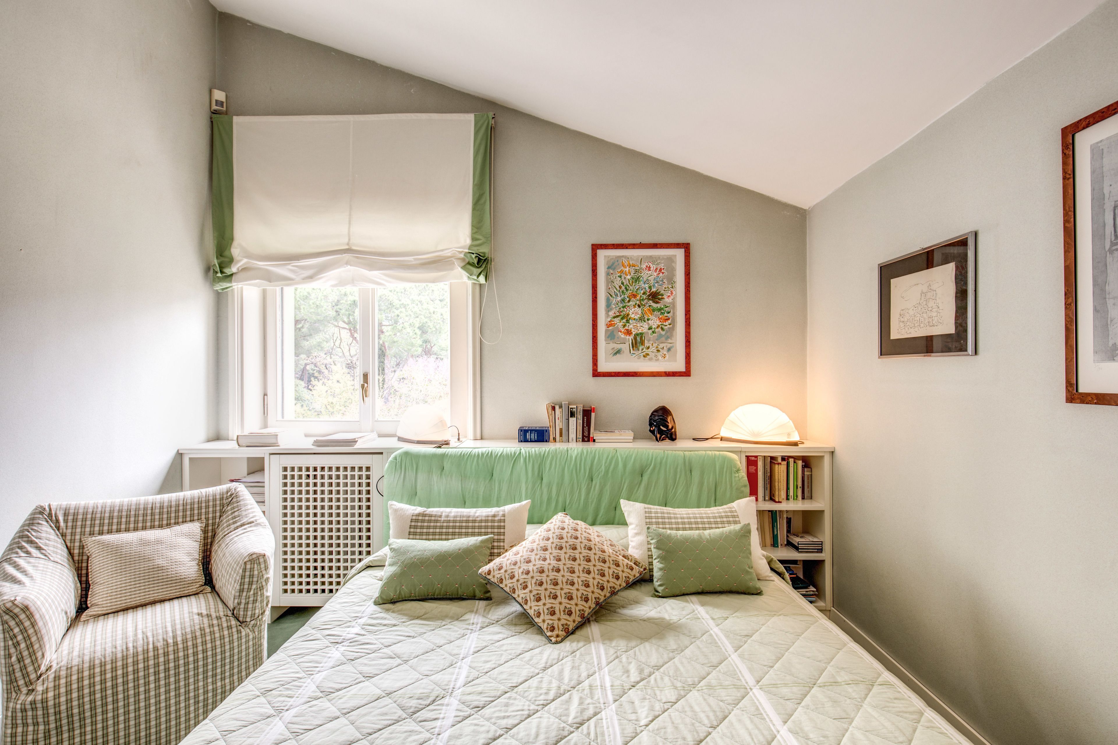 A bedroom with a bed, a chair, a desk, and a window with curtains.