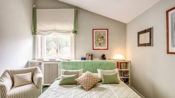 A bedroom with a bed, a chair, a desk, and a window with curtains.