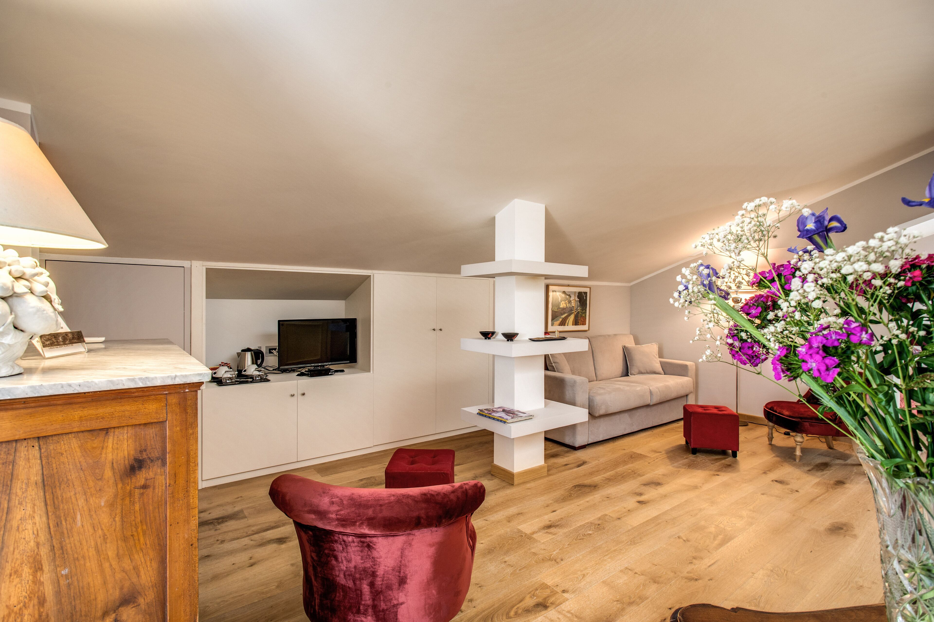 Uma sala de estar moderna com piso de madeira, uma cadeira vermelha, um sofá branco, uma televisão e um vaso com flores.