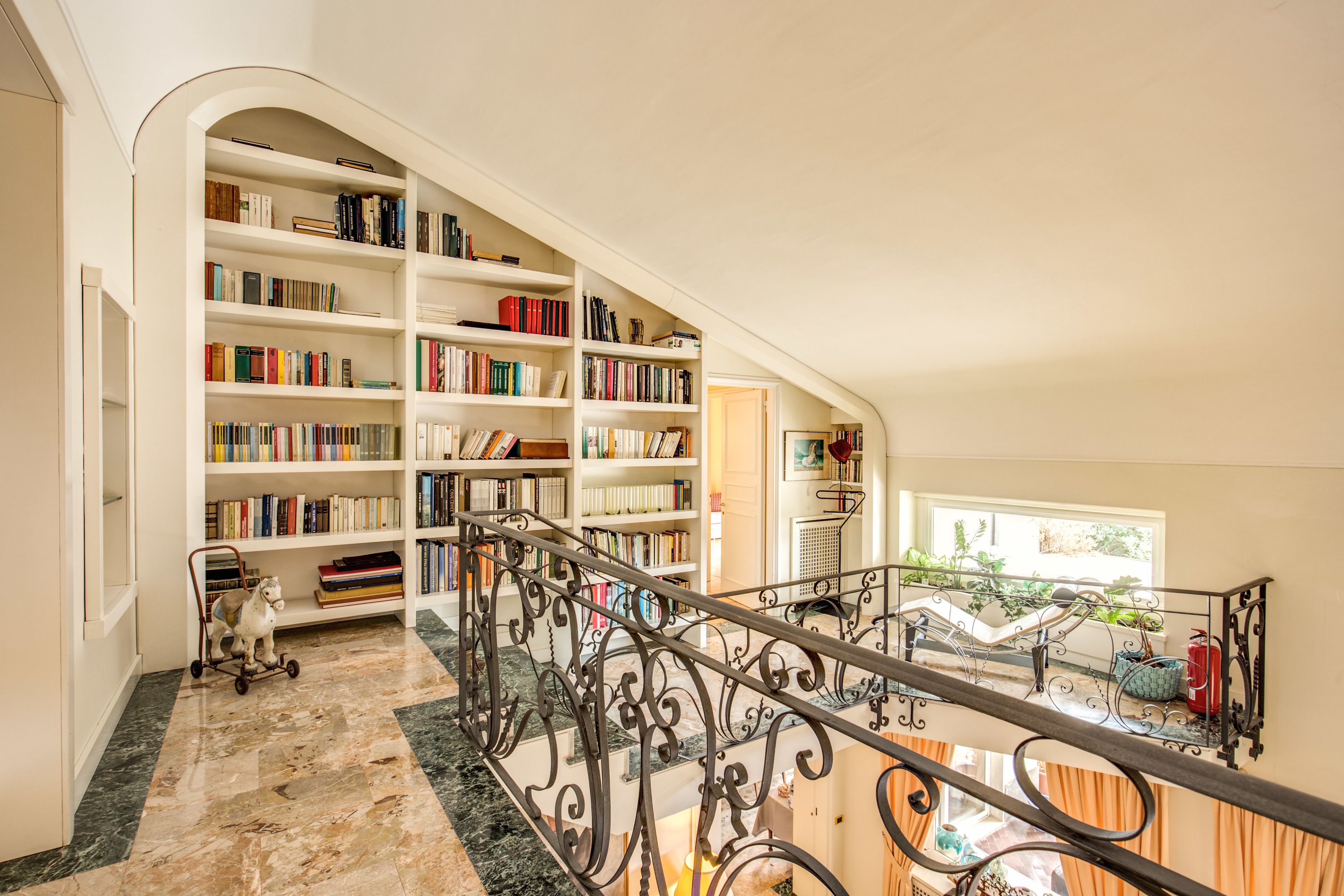 Une bibliothèque spacieuse, dotée d’étagères hautes, d’un sol en marbre et d’une balustrade en fer forgé.