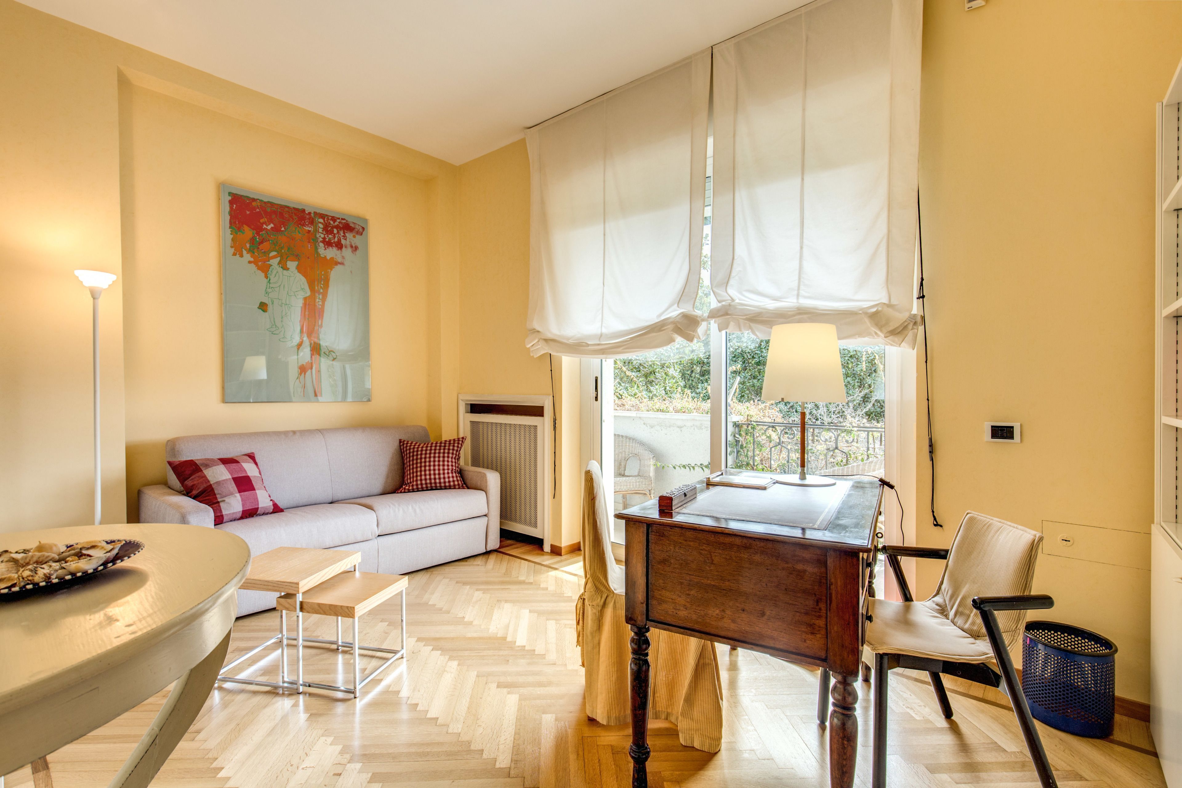 A living room with a sofa, a dining table, a chair, a lamp, and a window with curtains.