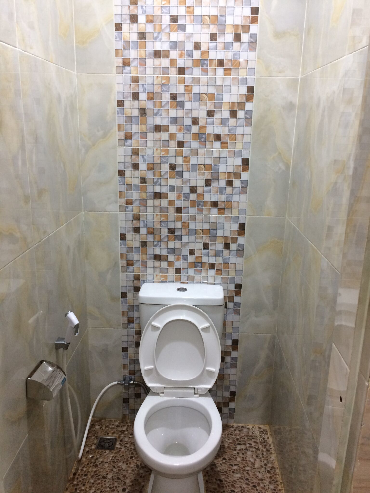 A bathroom with a toilet, a tiled wall, and a marble floor.