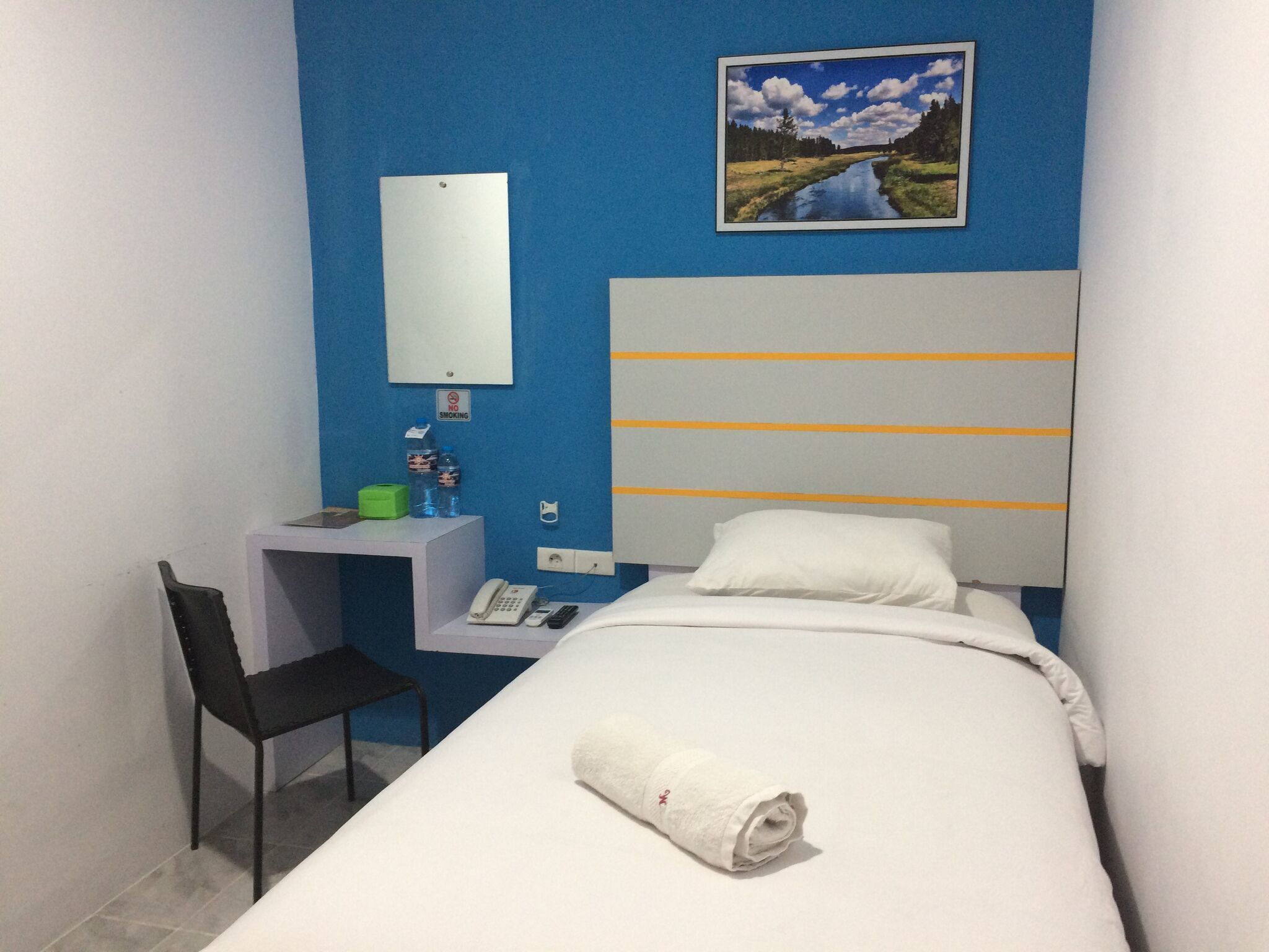 Ein Hotelzimmer mit einem Bett, einem Schreibtisch mit Stuhl, einem Telefon und einem Gemälde an der Wand.