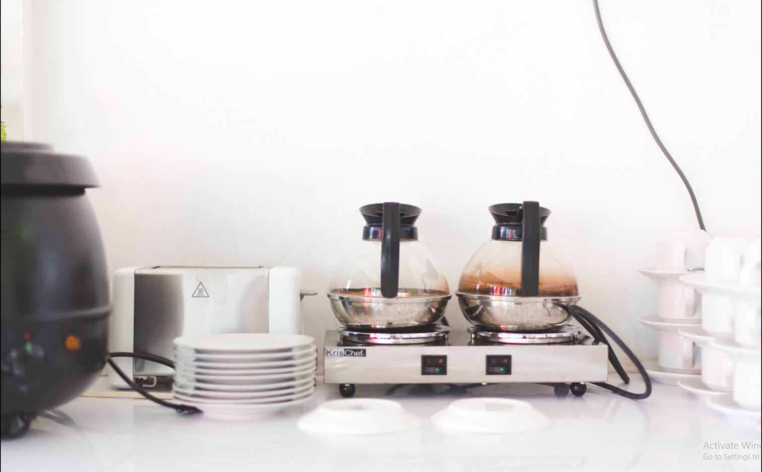 A kitchen with two electric kettles, a coffee maker, and a stack of plates.