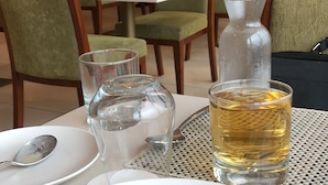 Une table à manger avec une assiette de nourriture, un verre d’eau et une bouteille de spiritueux.