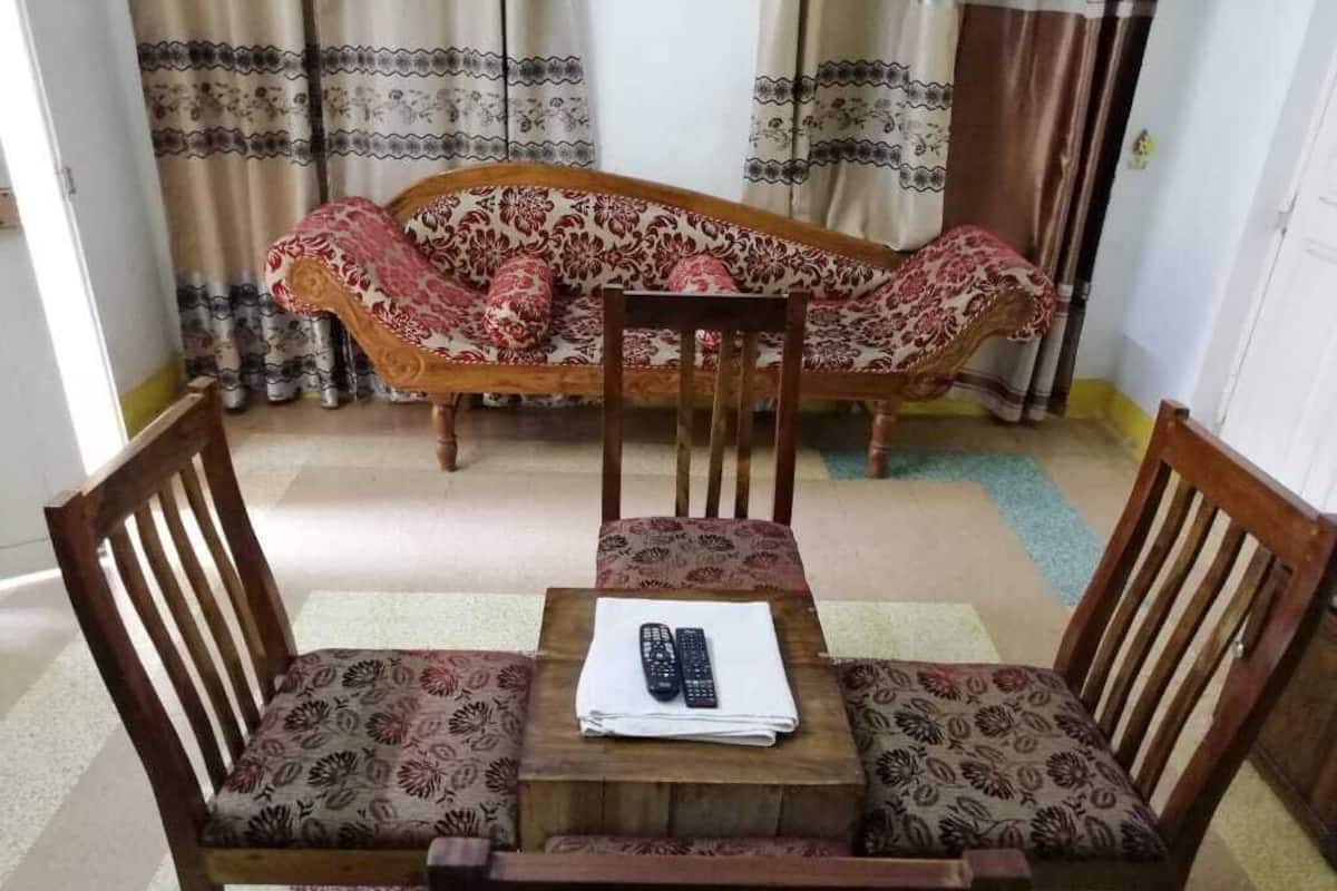 A room with a sofa and two wooden chairs around a small table with a remote control.