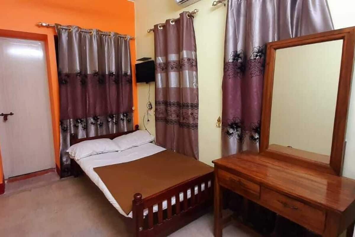 A bedroom with a bed, a wooden dresser, a mirror, and curtains.