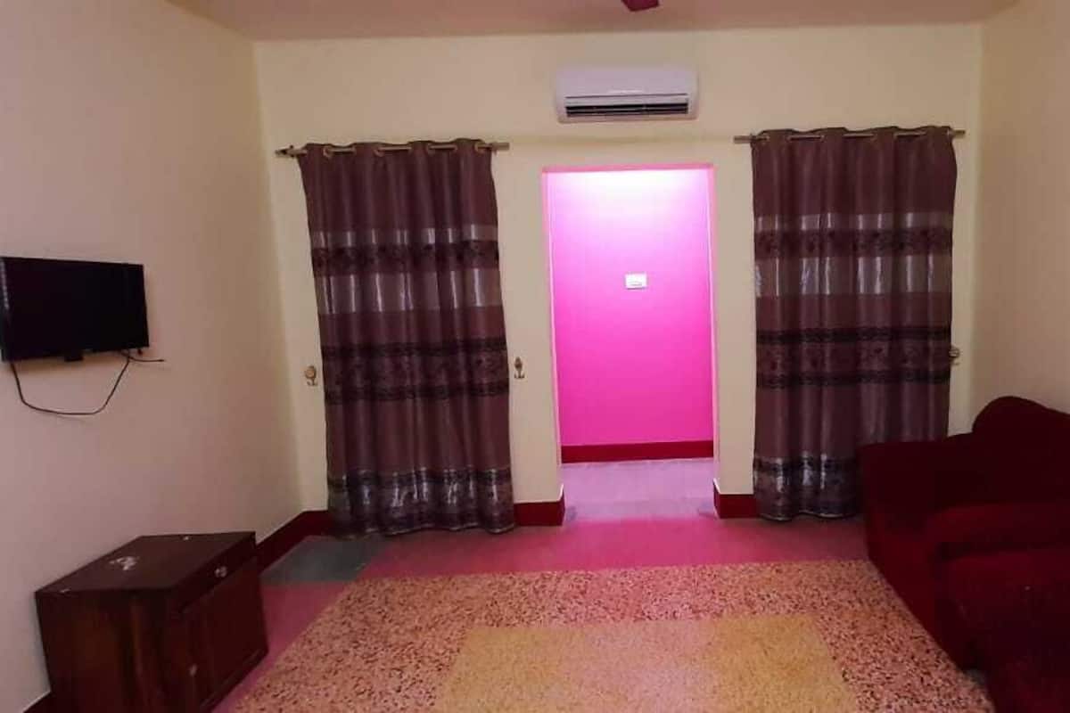 A living room with a red sofa, a television on the wall, and a pink-lit hallway.