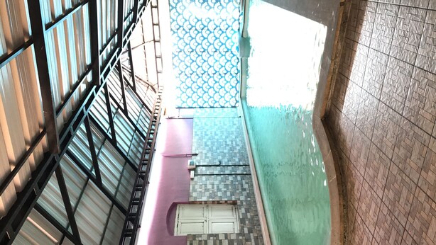 Un couloir intérieur doté d’un sol carrelé, d’une rambarde en métal et d’un plafond orné de motifs.