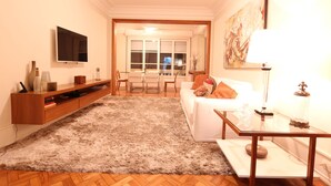 Ein Wohnzimmer mit Flachbildfernseher, einem weißen Sofa, einem Glastisch und einem flauschigen Teppich.