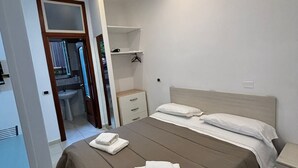 A bedroom with a bed, bedside tables, a wardrobe, and a bathroom visible through an open door. - Home To Fly (Naples)
