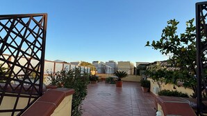 A rooftop terrace with a tiled floor, potted plants, and a view of buildings in the distance. - Home To Fly (Naples)