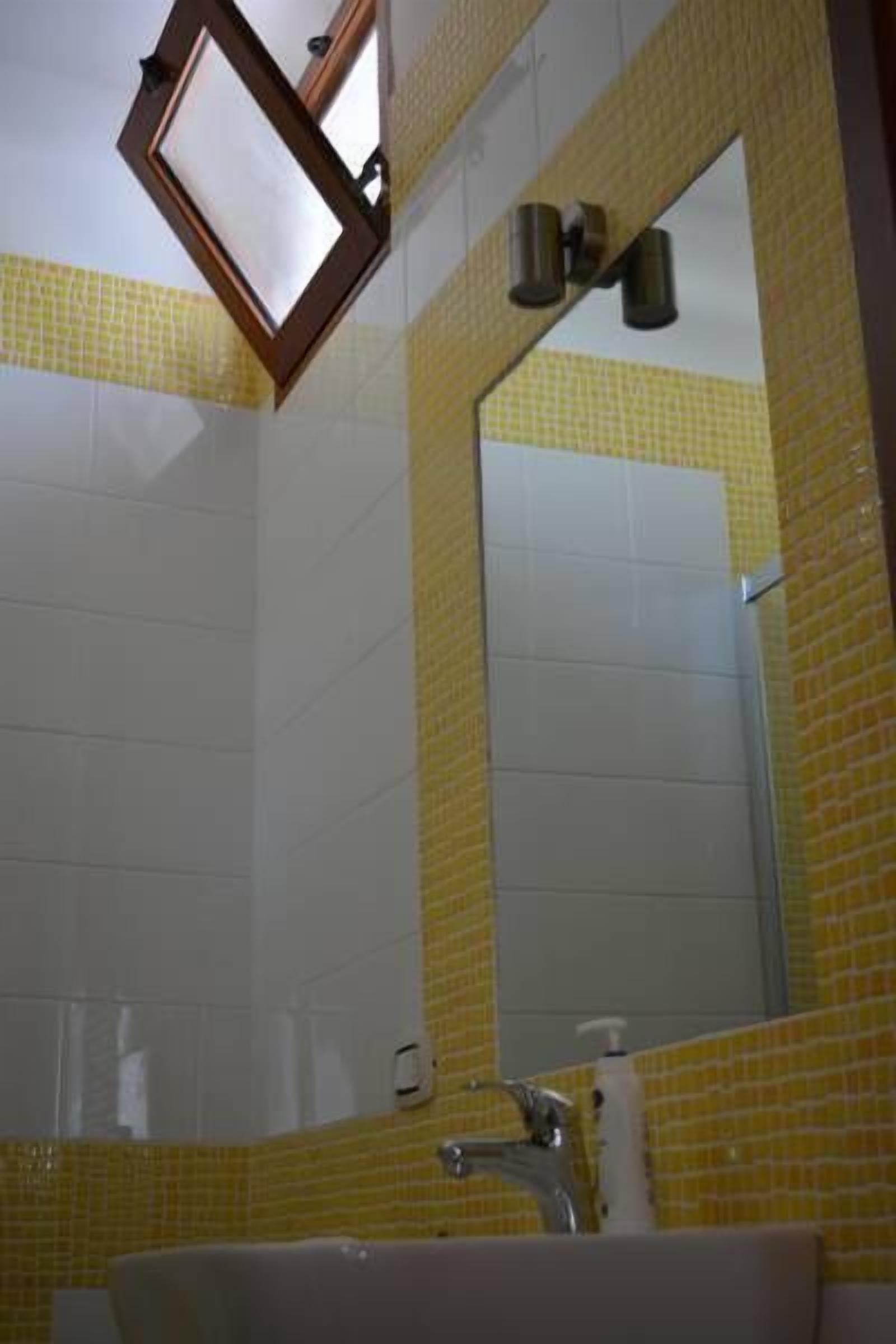 Ein Badezimmer mit gelb gefliesten Wänden, einem weißen Waschbecken und einem Spiegel mit Holzrahmen.