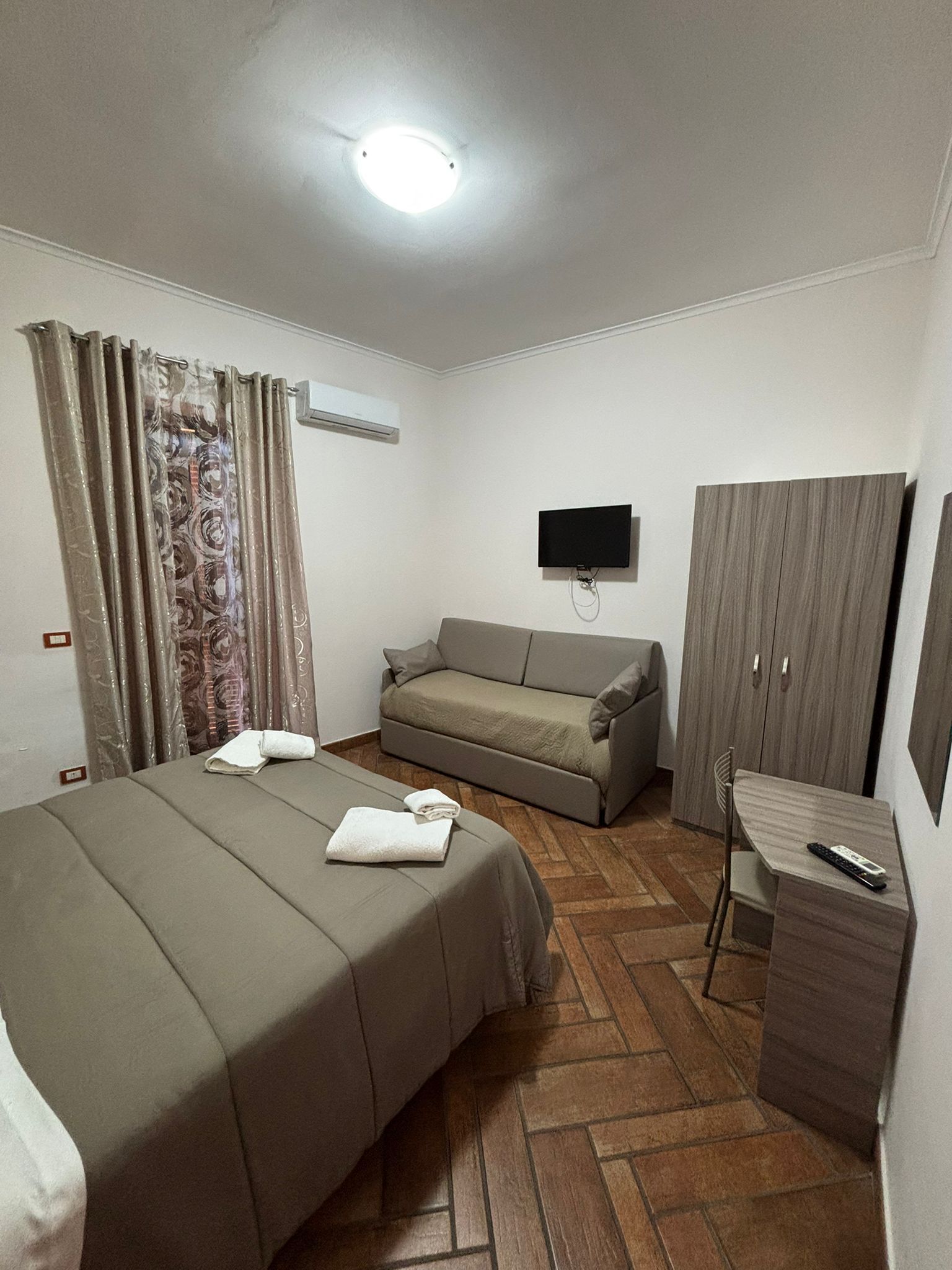 A hotel room with a bed, a sofa, a desk, a TV, and a wardrobe.