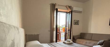 A hotel room with two beds, a radiator, an air conditioning unit, and a view of the outside balcony.
