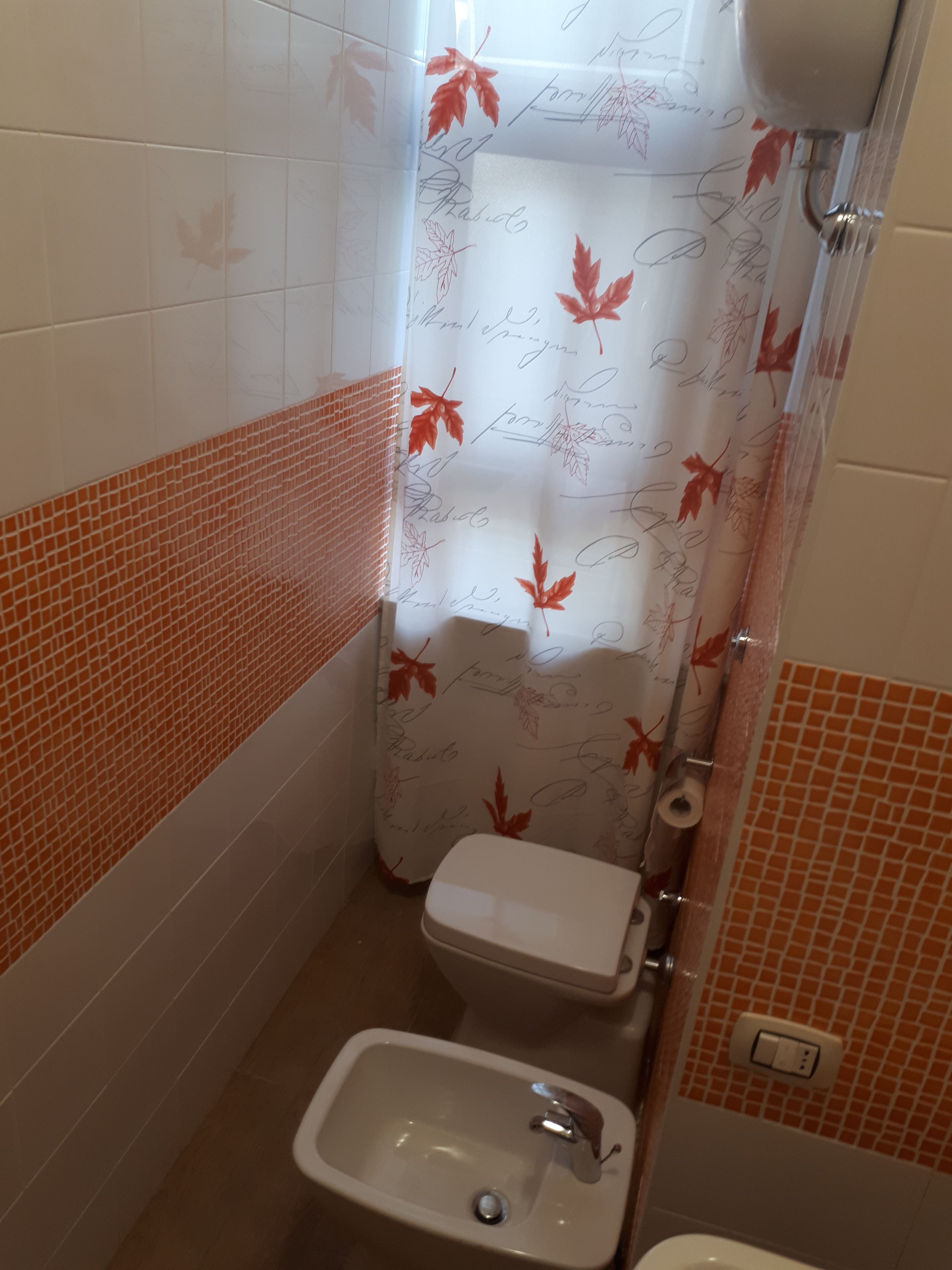 Een kleine badkamer met toilet, wastafel en douchegordijn met bladmotieven.