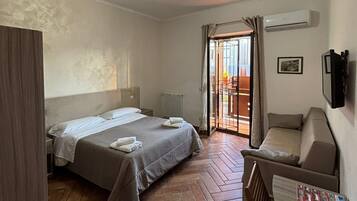 Una habitación de hotel con cama, sofá, televisión y ventana con cortinas.