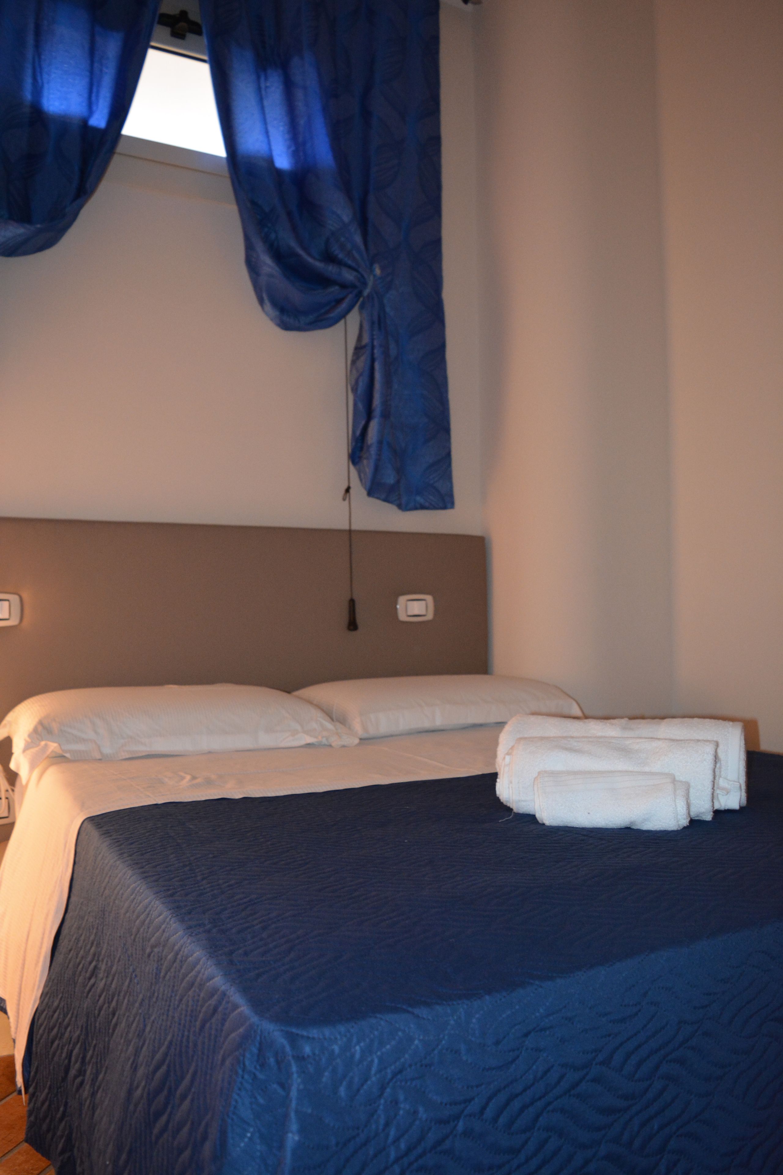 Un dormitorio con dos camas, una ventana con cortinas azules y un cabecero.