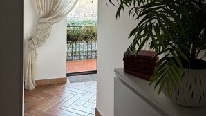 A hallway with a potted plant, a window with curtains, and a tiled floor. - Home To Fly (Naples)