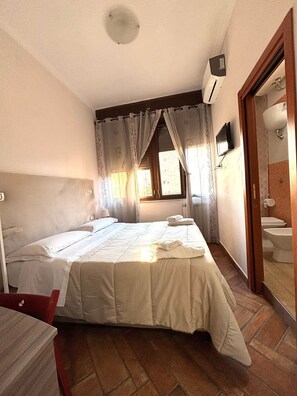Un dormitorio con una cama grande, televisión y baño con inodoro y lavabo.