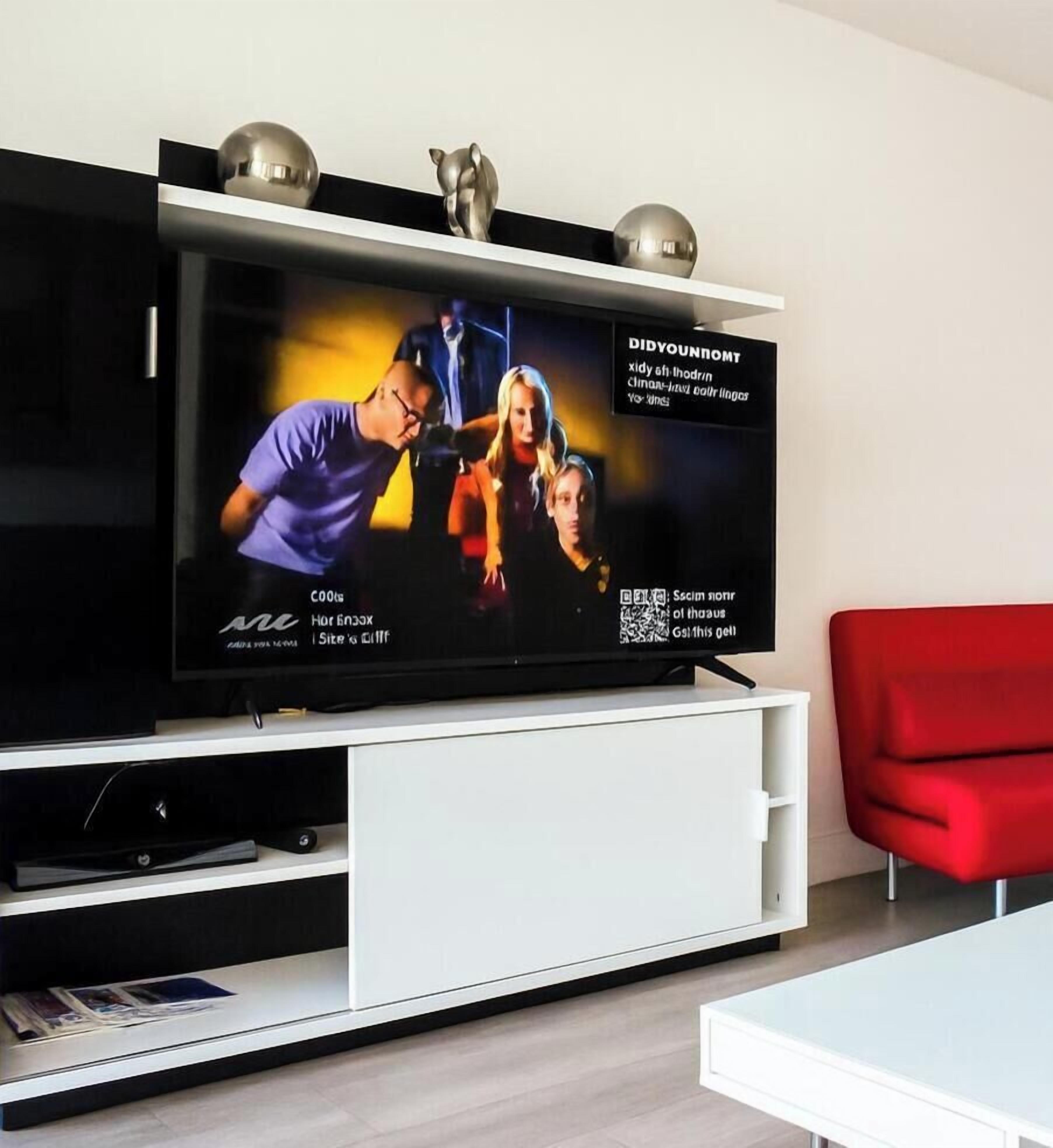 Ein Flachbildfernseher auf einer weißen Unterhaltungseinheit mit einem roten Sessel in der Nähe.