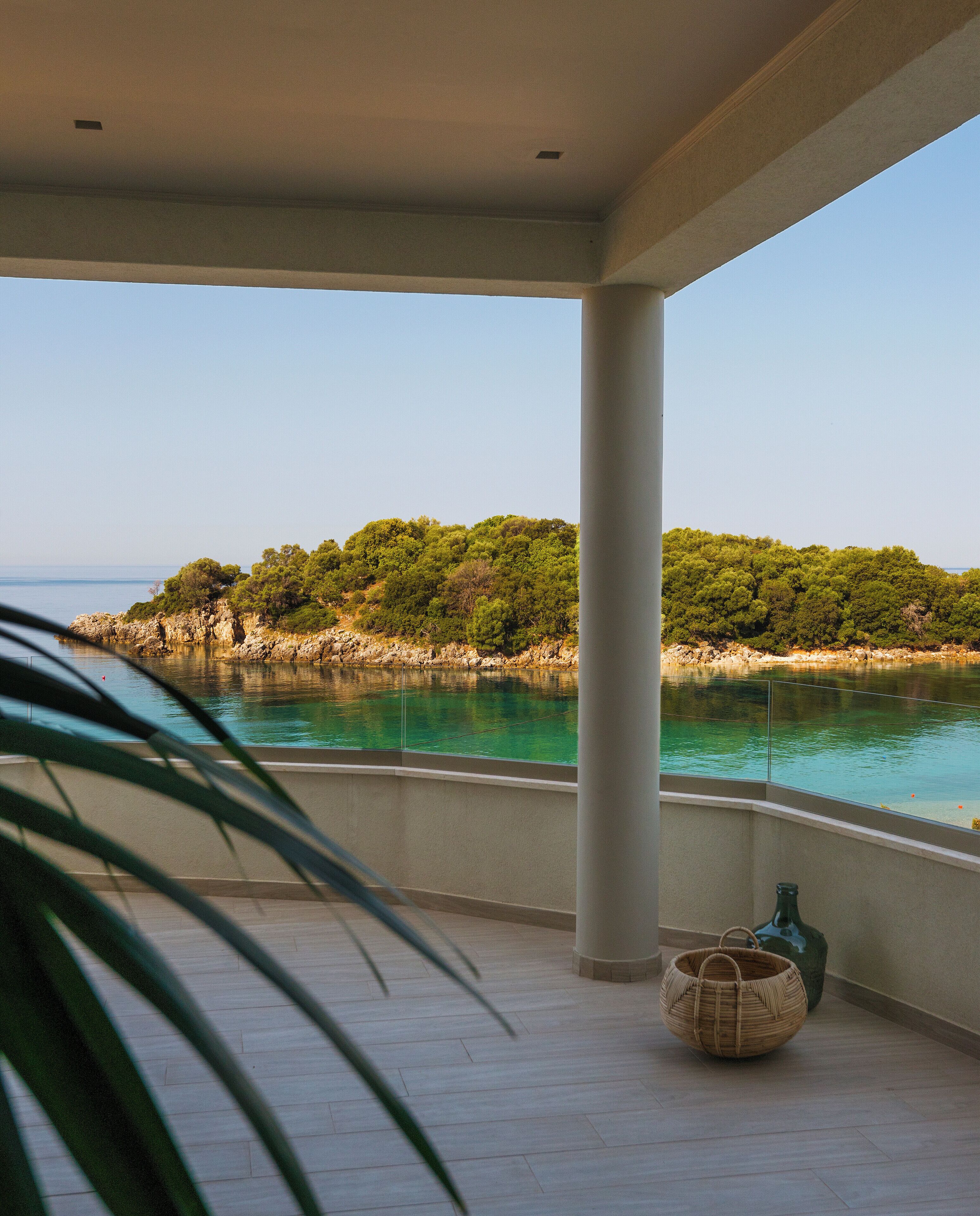 Un balcón con vista a un paisaje costero, cielo despejado y mar tranquilo.