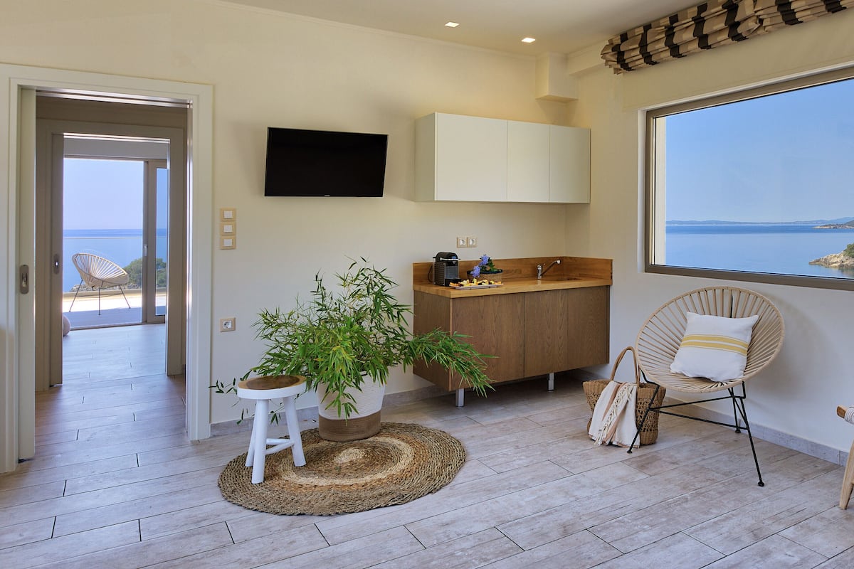 Una cocina moderna con un ventanal grande, un rincón de comedor con una silla de mimbre y vista al mar.