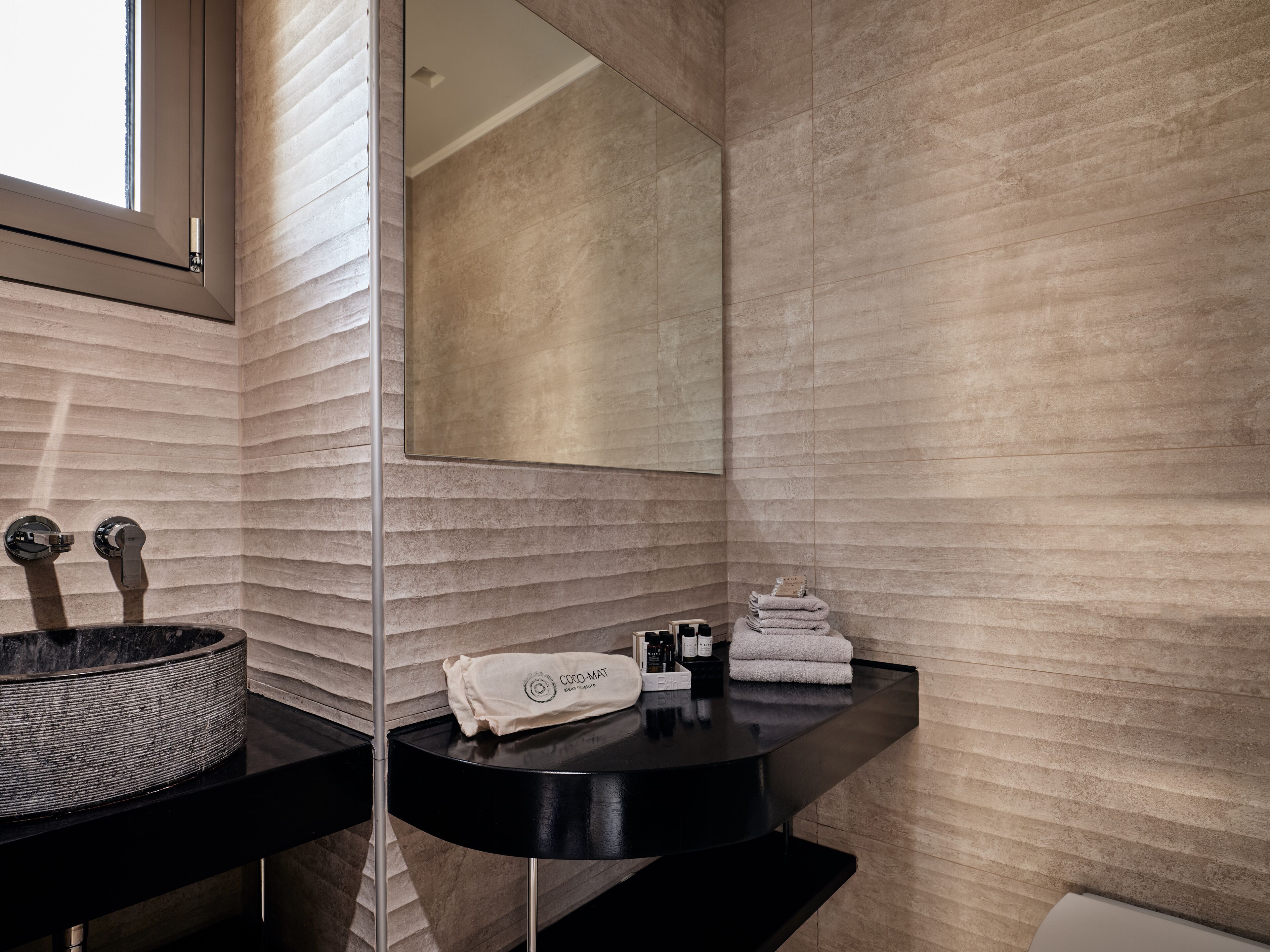 A modern bathroom with a black sink, a large mirror, and a textured wall.