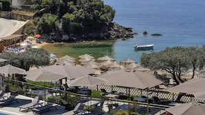 A resort with a swimming pool, lounge chairs, umbrellas, and a view of the sea and a rocky island.