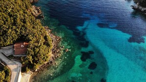 An aerial view of a coastal area with a clear beach, rocky shoreline, and a small boat.