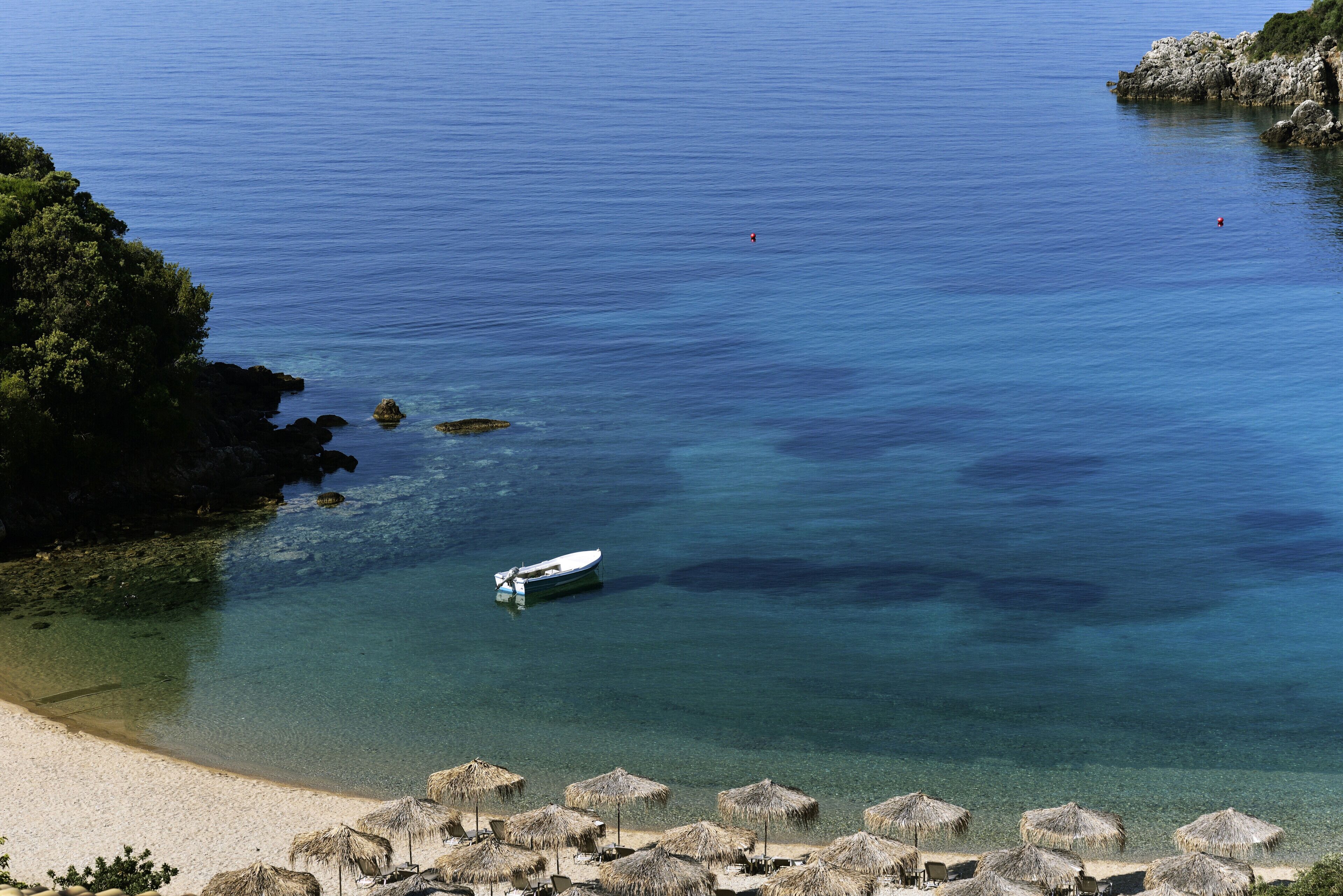 A beach with clear water, a boat, and thatched umbrellas.