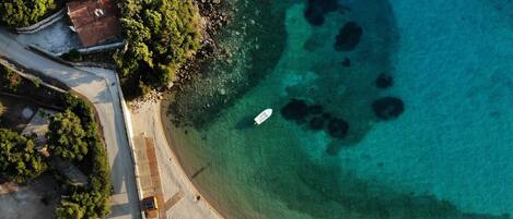 Vista aérea de una playa con aguas turquesas cristalinas, un bote y una fila de sombrillas.
