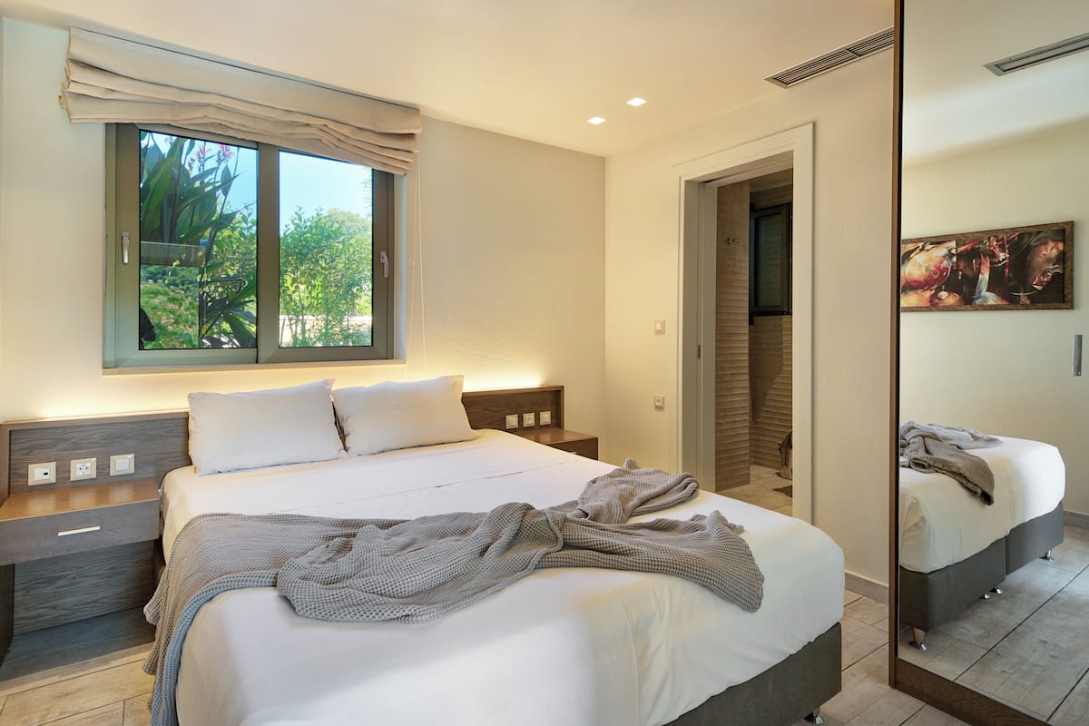 Un dormitorio con una cama grande, mesitas de noche, una ventana con cortinas y un espejo.