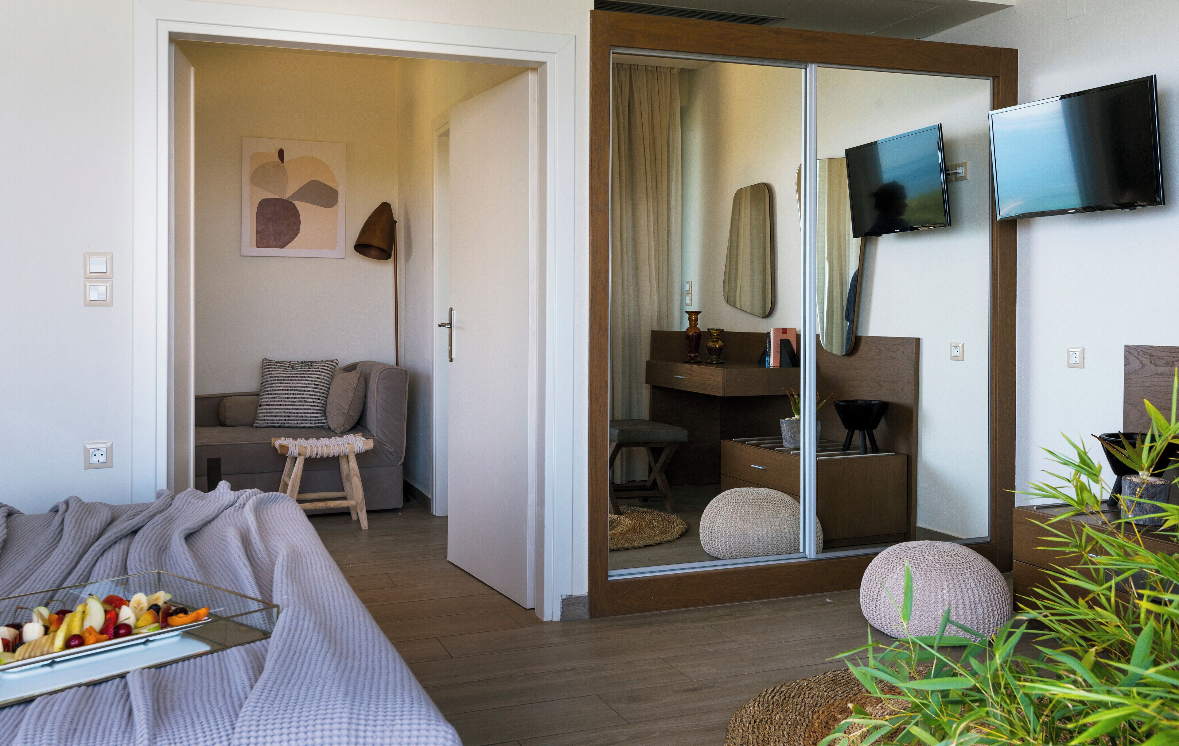 Een moderne hotelkamer met een bed, een zithoek met een bank en fauteuil, een eettafel en een aan de muur bevestigde televisie.
