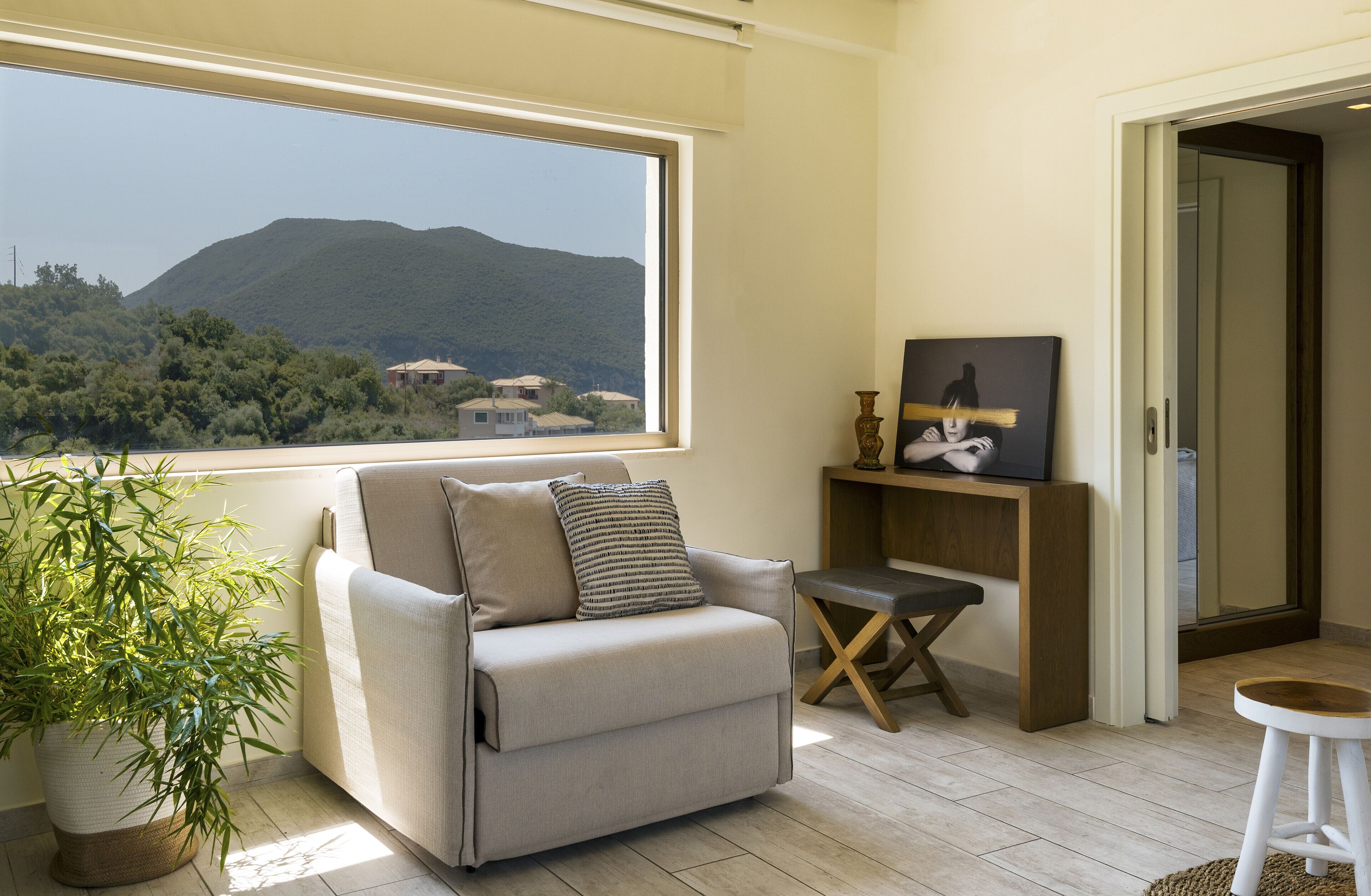 Una habitación con un sofá, una pequeña mesa, una planta en maceta y vistas a una montaña.