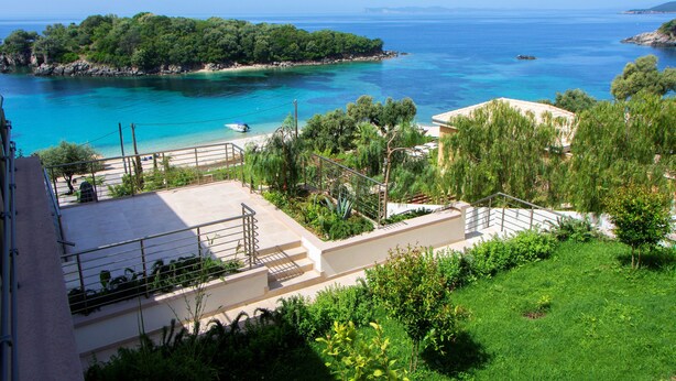 A coastal view with a clear blue sea, a small island with dense greenery, and a building with a balcony overlooking the sea.