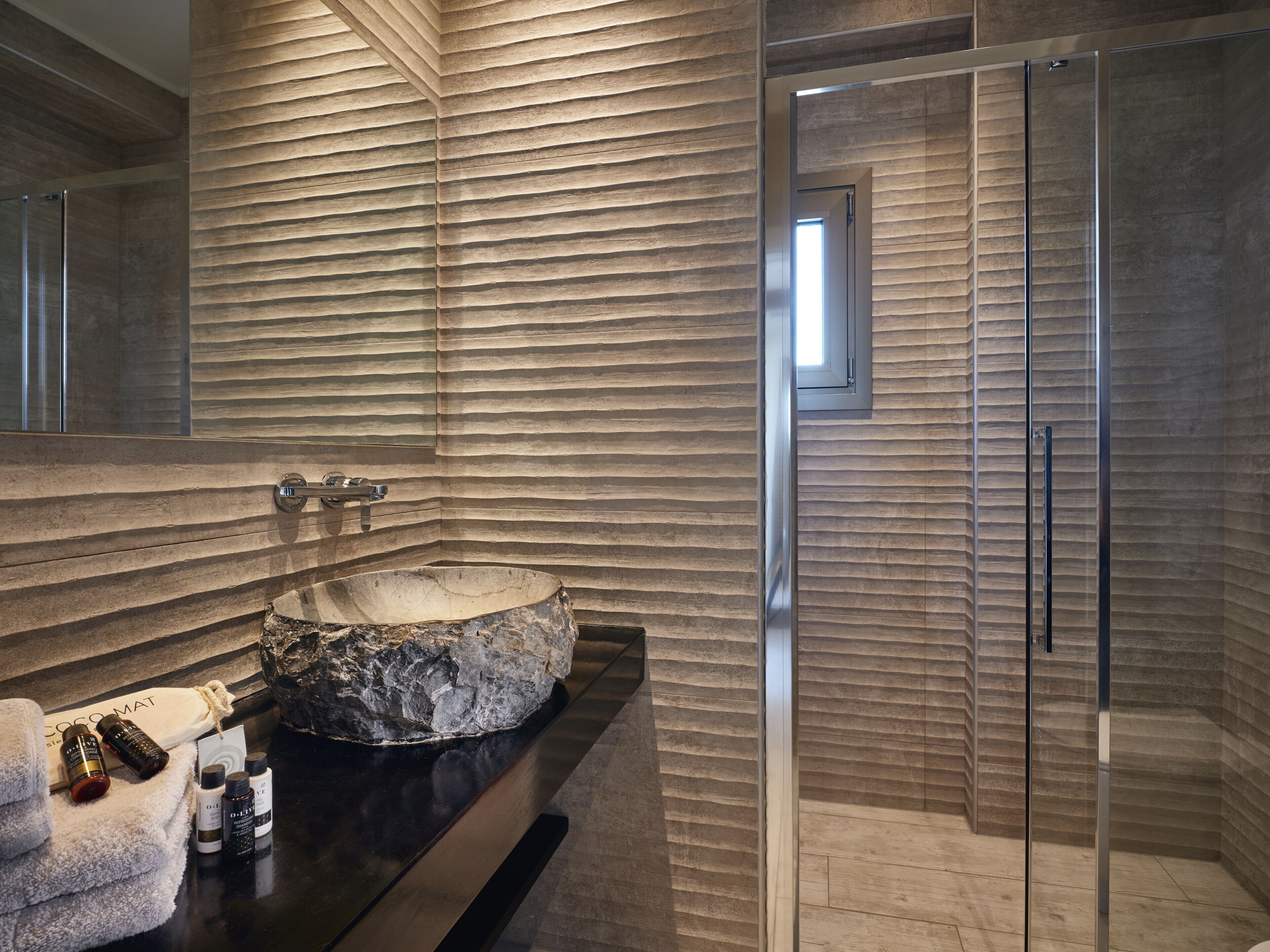 Een moderne badkamer met een groot stenen wastafel, een douchecabine met glazen wanden en een wand van hout met structuur.