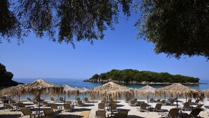 A beach with sun loungers and thatched umbrellas, a stone pathway, and a view of the sea and a small island.
