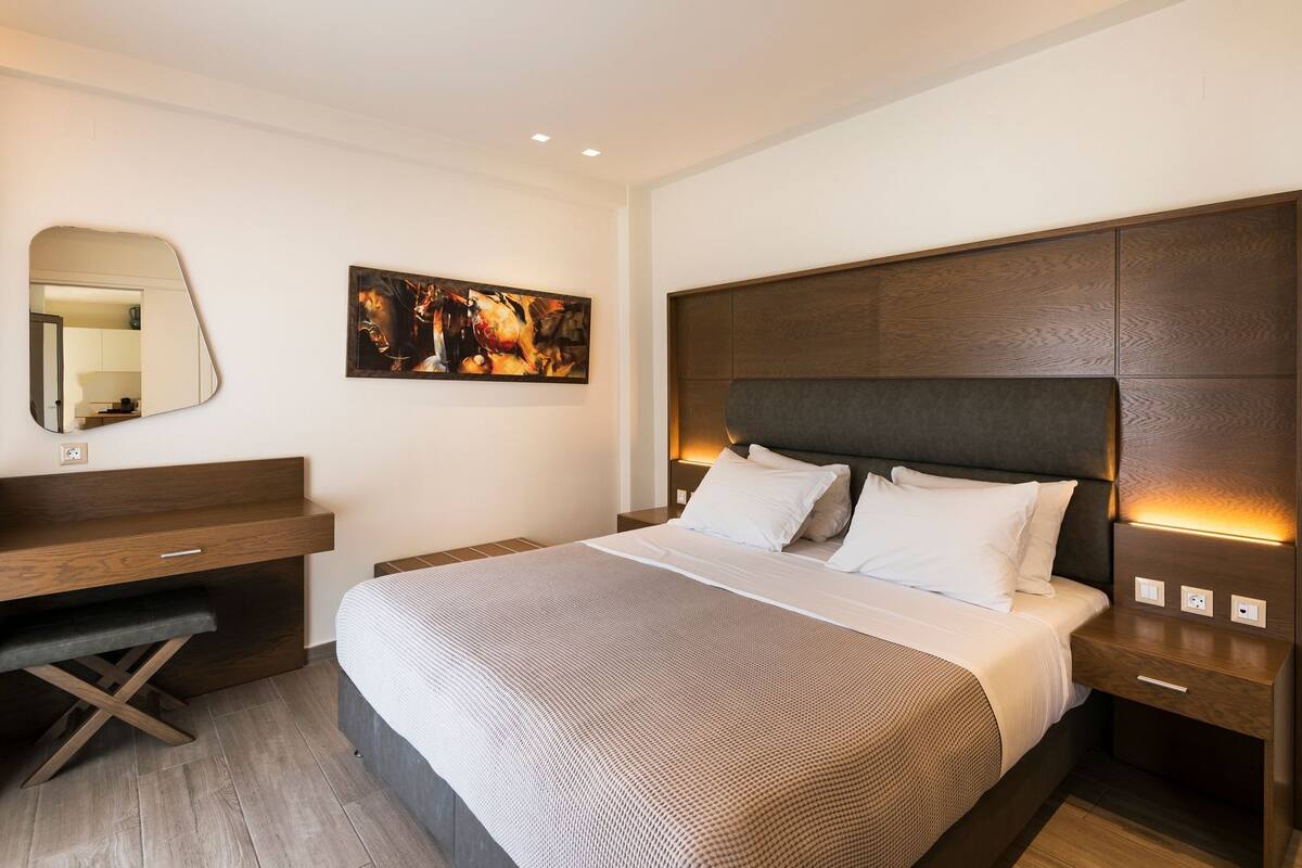 Una habitación de hotel moderna con una cama grande, un escritorio, un espejo y un cuadro en la pared.