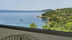 A room with a large window overlooking a coastal landscape, including a body of water and a hillside with vegetation.