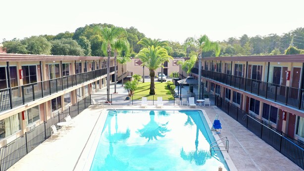 A pool area with a rectangular pool, surrounded by a low fence, and adjacent to a row of motel-style buildings with balconies.