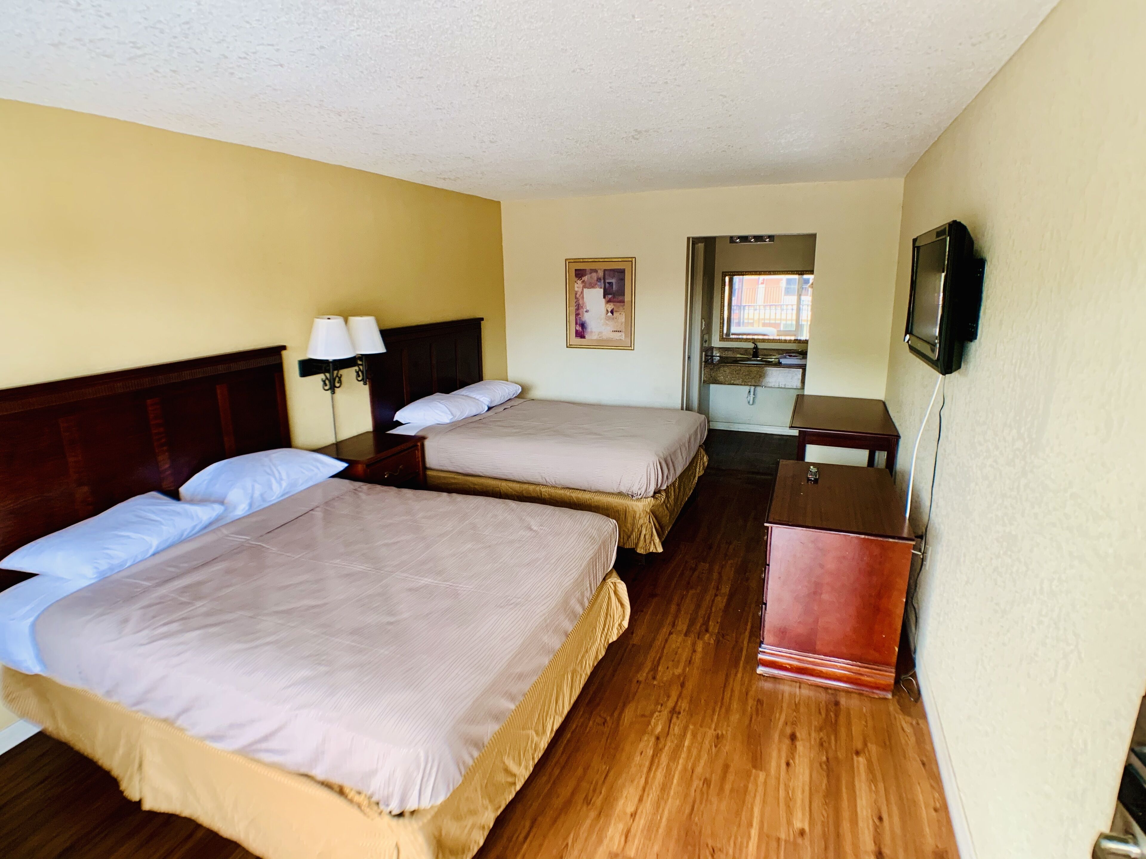 A hotel room with two beds, a small desk, a television, and a window.