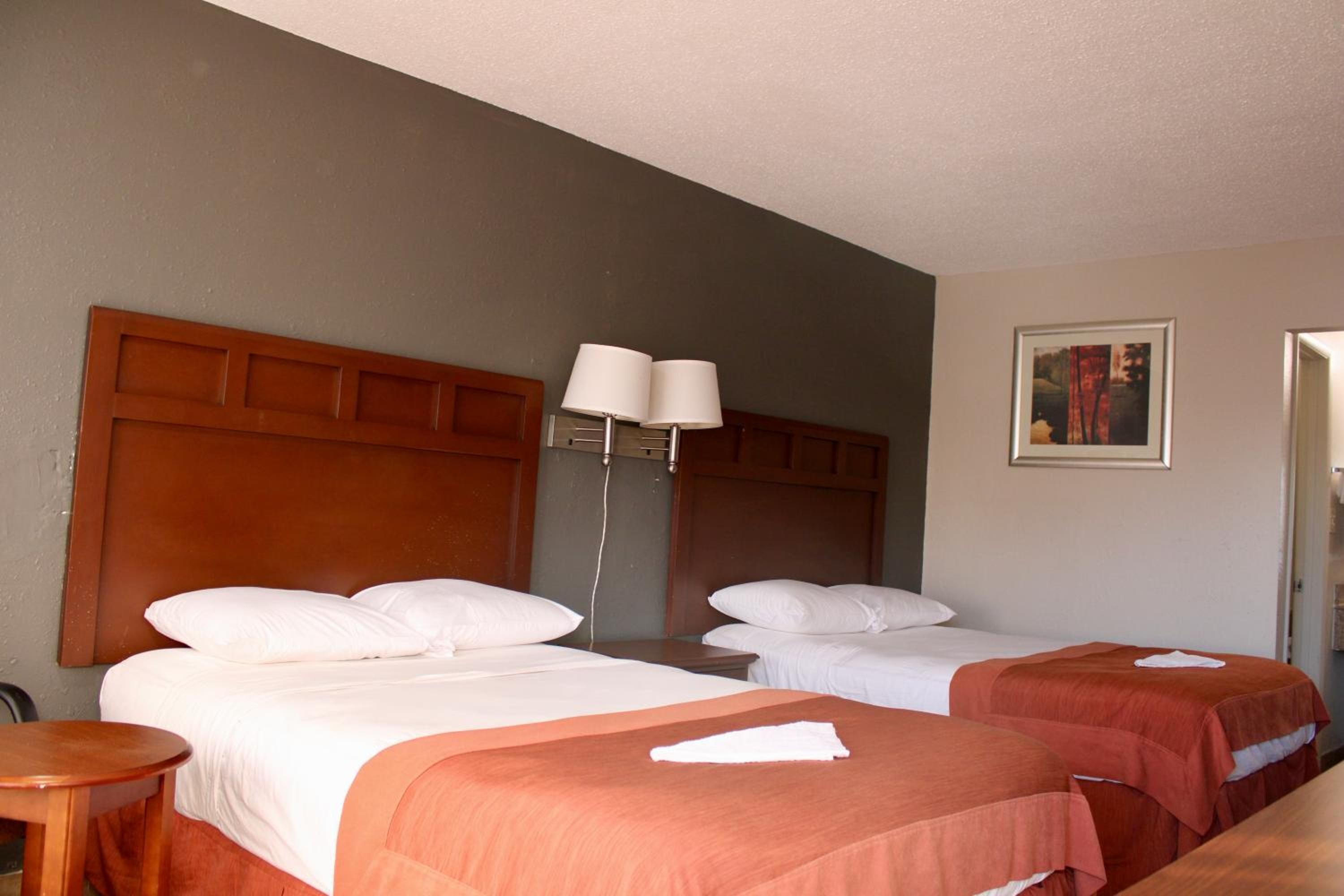 Una habitación de hotel con dos camas, una mesita de noche, una lámpara y un cuadro en la pared.