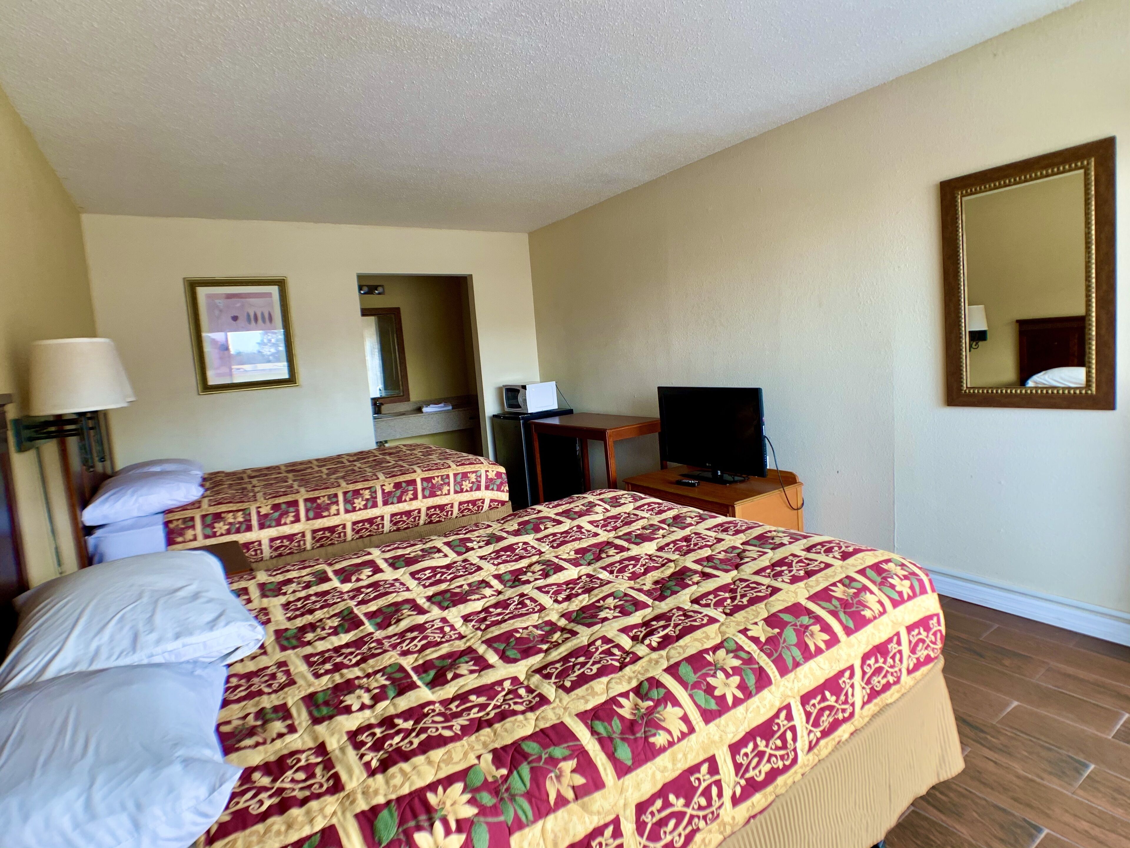 A hotel room with two beds, a television, a desk, and a mirror.