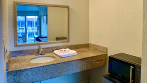 A bathroom with a granite countertop sink, a mirror, a towel, and a compact refrigerator.