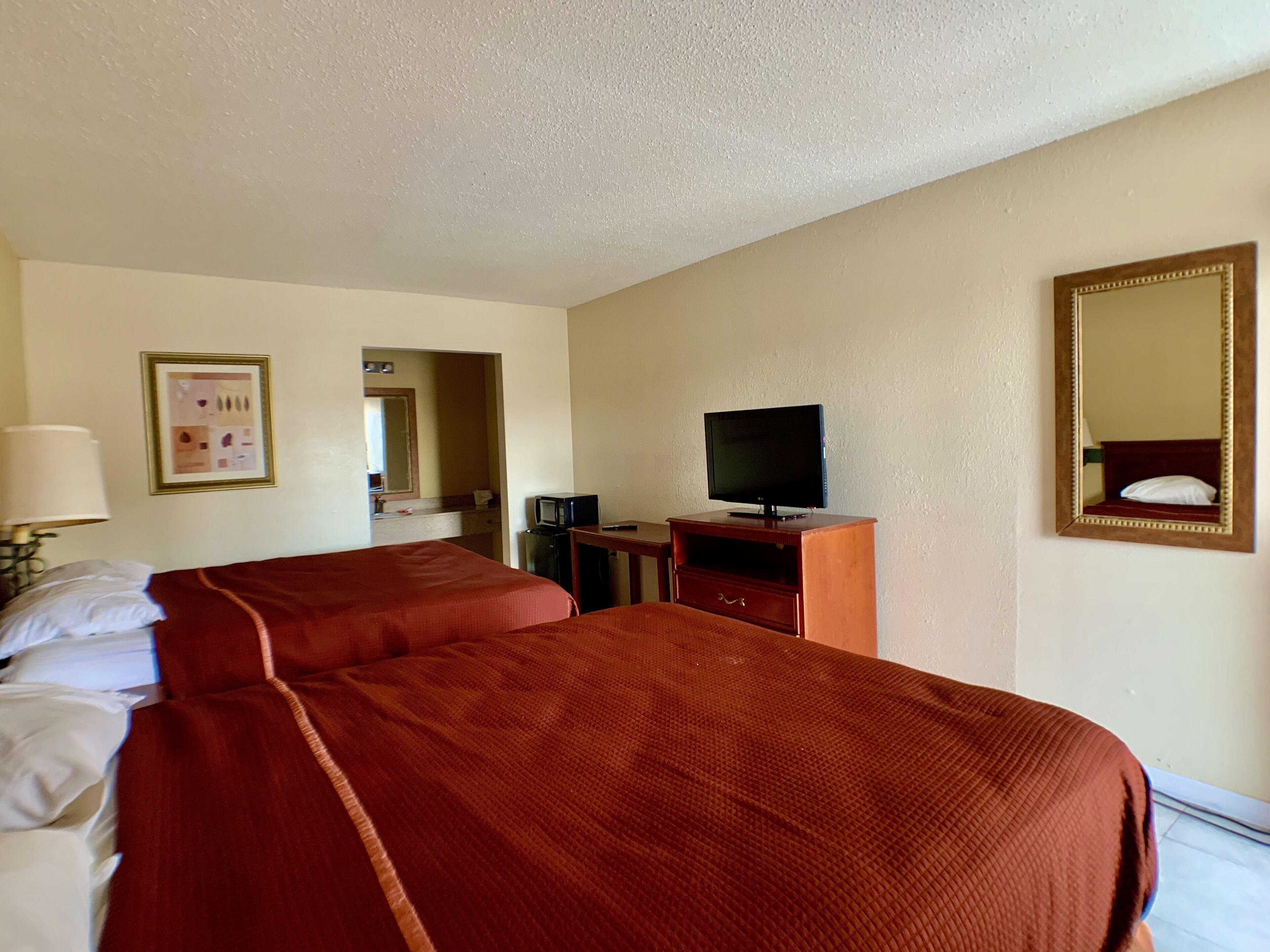 A hotel room with two beds, a television, a desk, a mirror, and a lamp.
