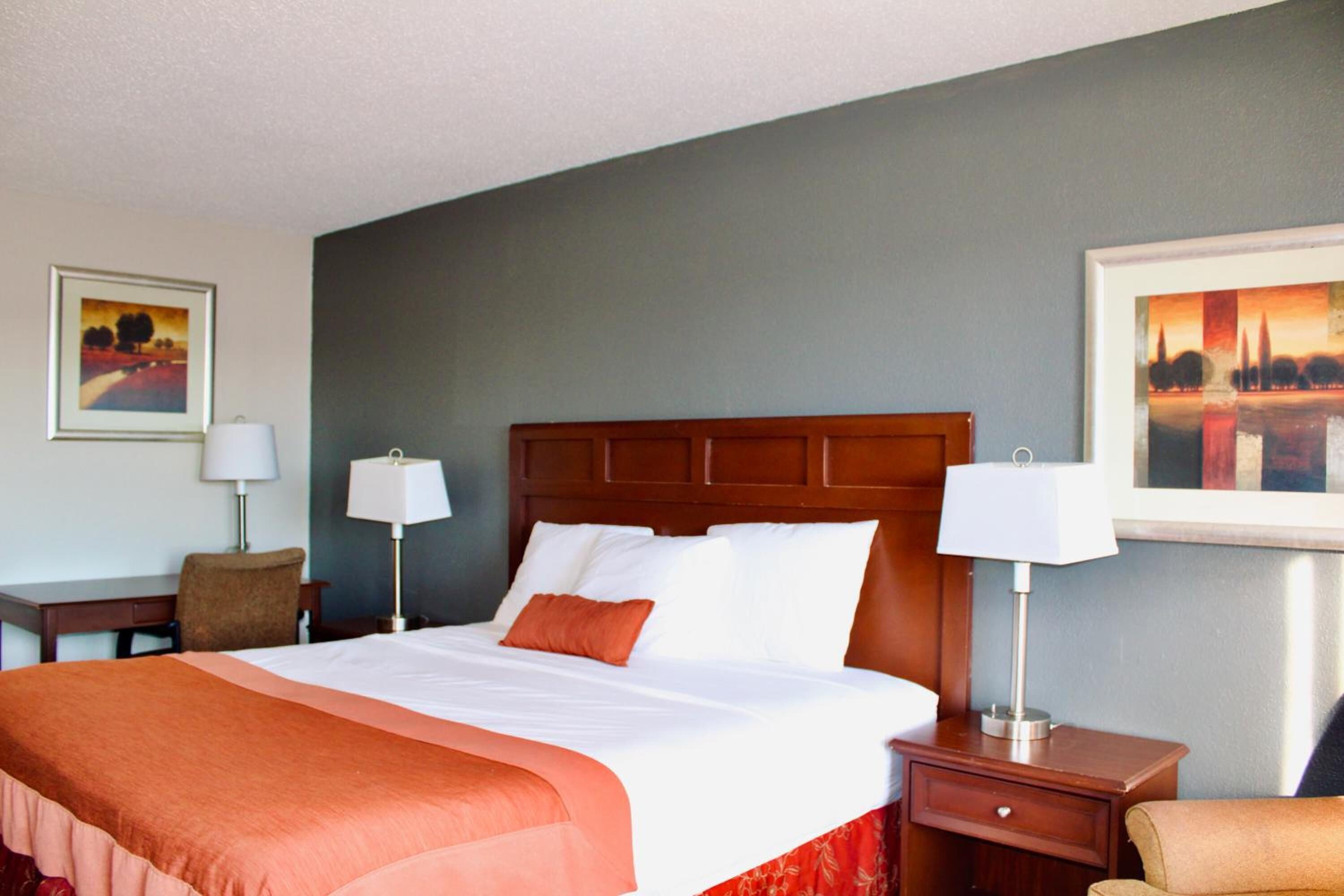 A hotel room with a large bed, two bedside tables with lamps, a chair, and artwork on the walls.