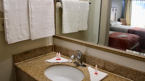 A hotel bathroom with a granite countertop sink, a mirror, and two towels hanging on a towel rack.